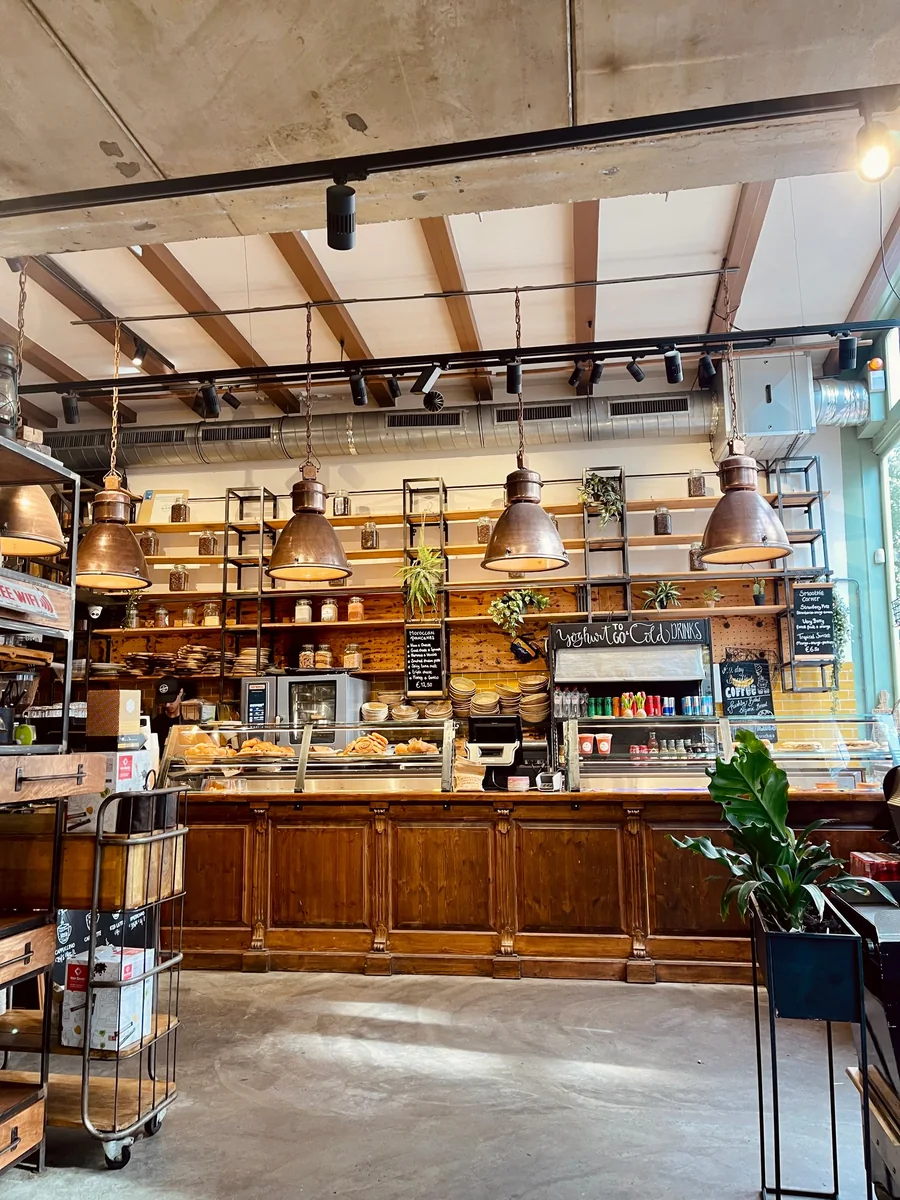 A warmly lit café with hanging copper lamps, a wooden counter, pastries, and green plants